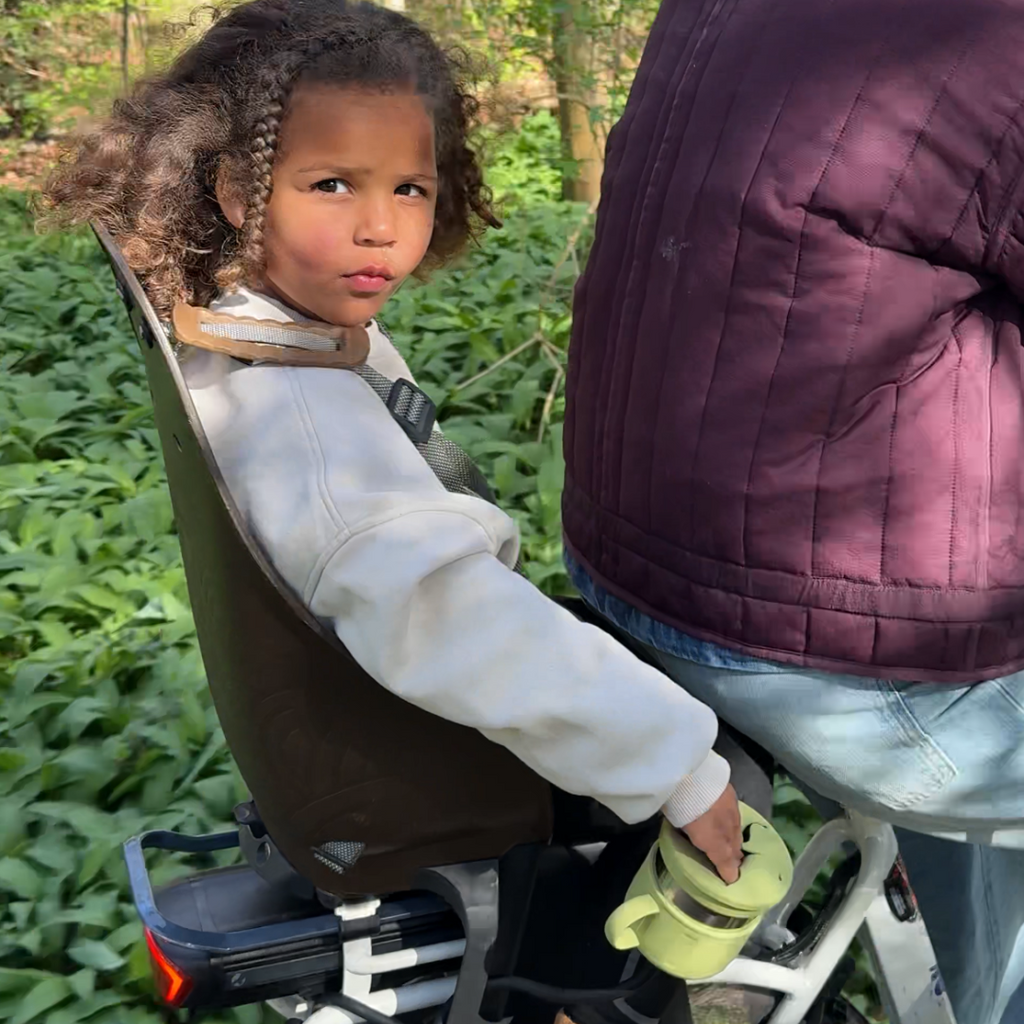 child on a bike reaching into a snack cup that is mounted to the bicycle