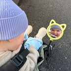 Baby toddler in a stroller with a green mirror showing a smiling baby's reflection.