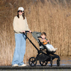 Woman pushing a stroller with a child with a mounted snack cup against a natural background